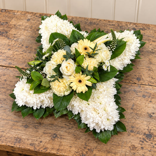 Massed Cushion with curved sides, white chrysanthemums and a cream and yellow flower spray on a rustic florist bench